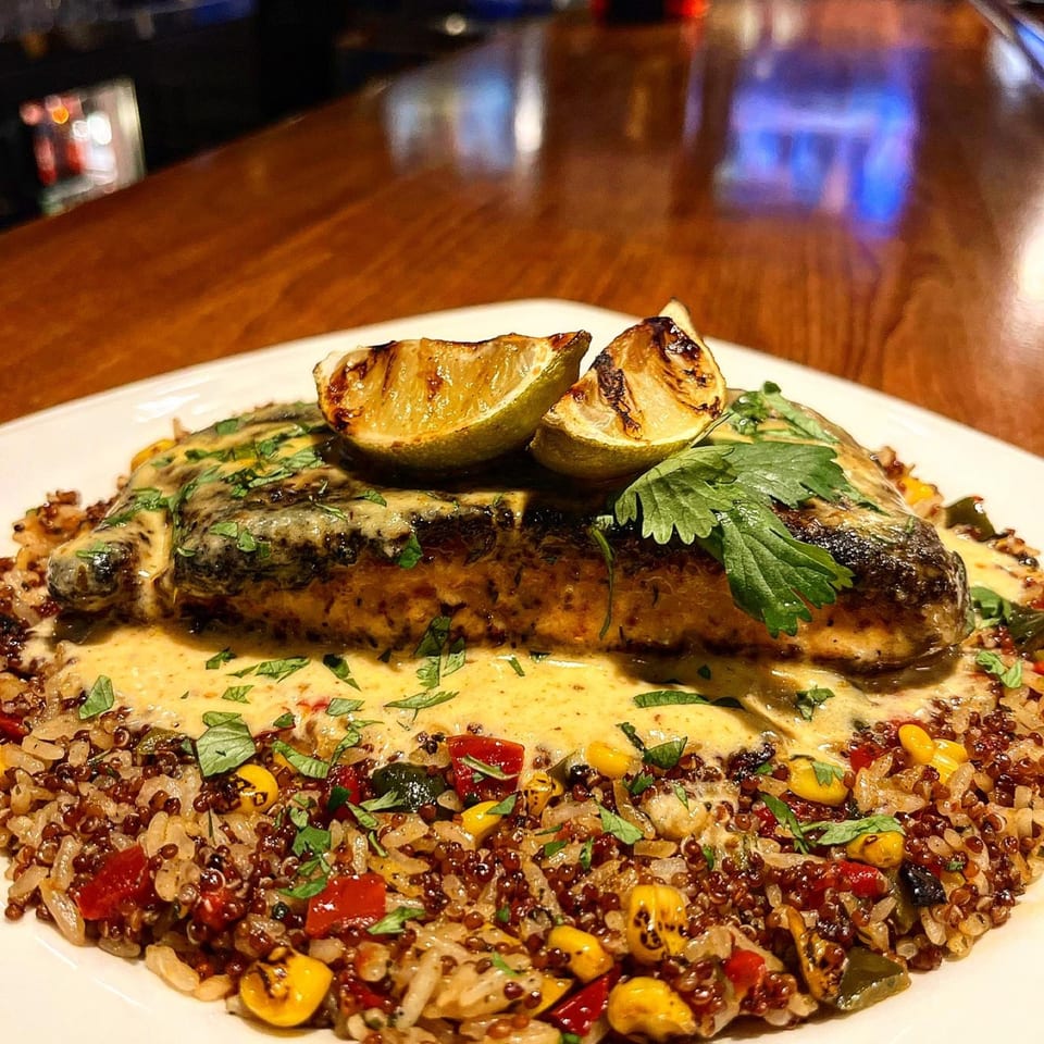 Grilled fish with creamy sauce, cilantro, and charred lime on a bed of quinoa and vegetables.