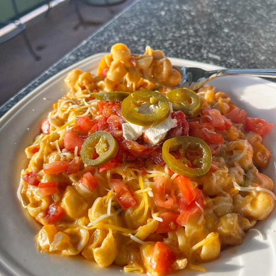 Cheesy macaroni with diced tomatoes, jalapeños, and a dollop of sour cream on a white plate.