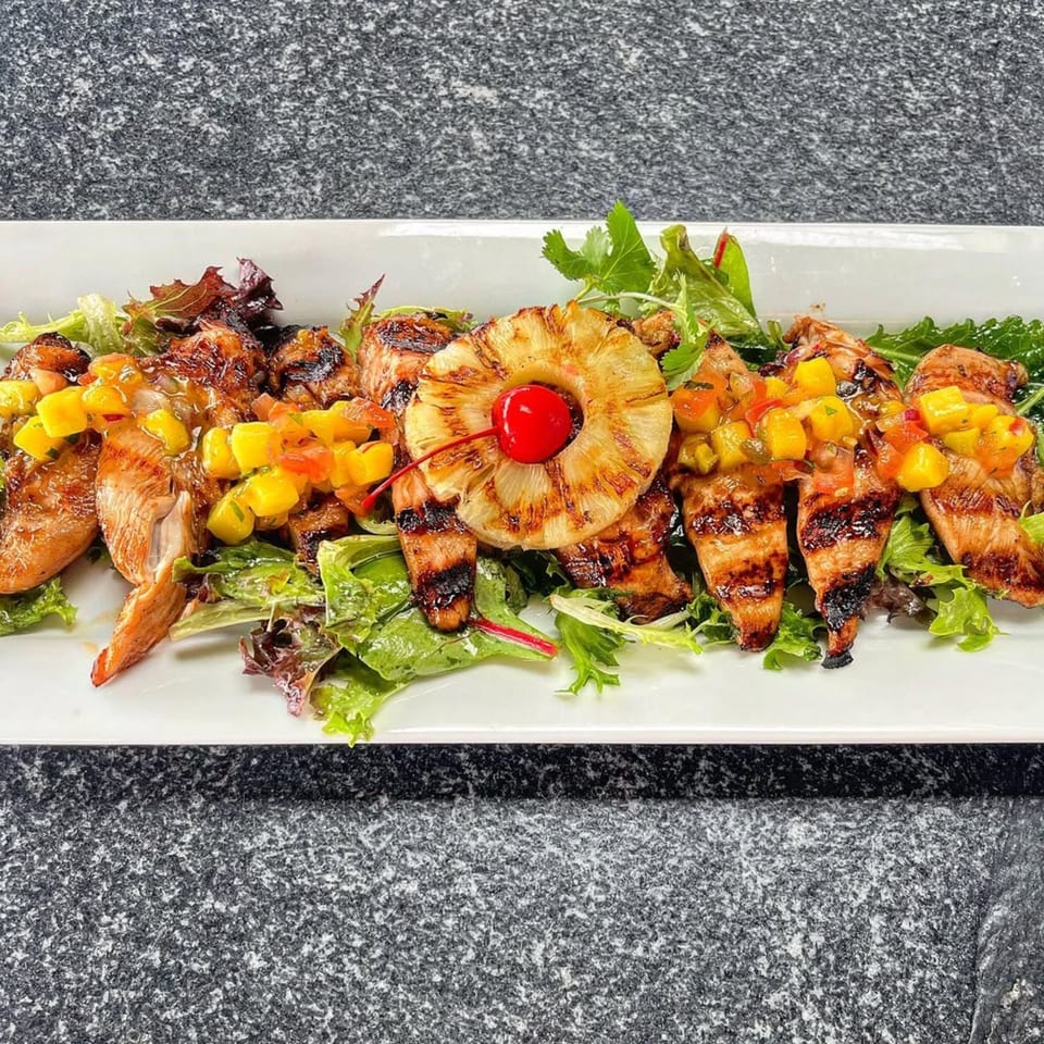 Grilled chicken strips with mango salsa and a pineapple ring with a cherry on a bed of greens.