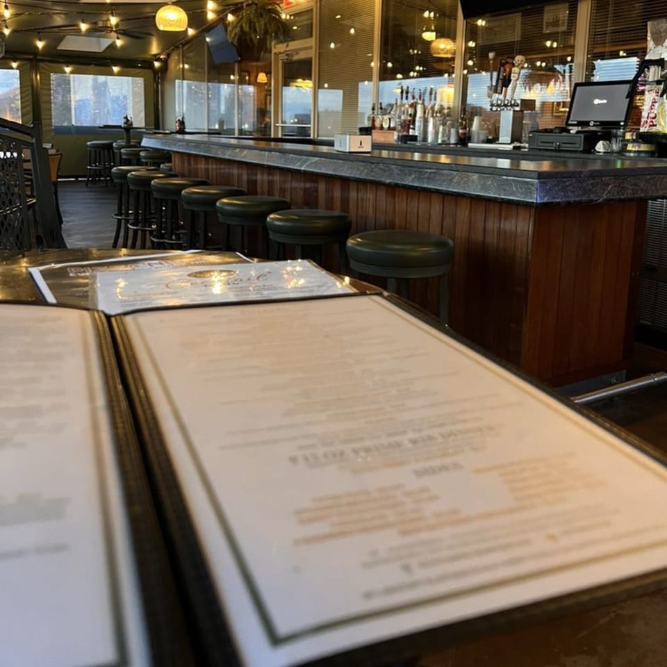 Open menu on a table with a long bar, stools, and bottles in the background at GS Steamers.