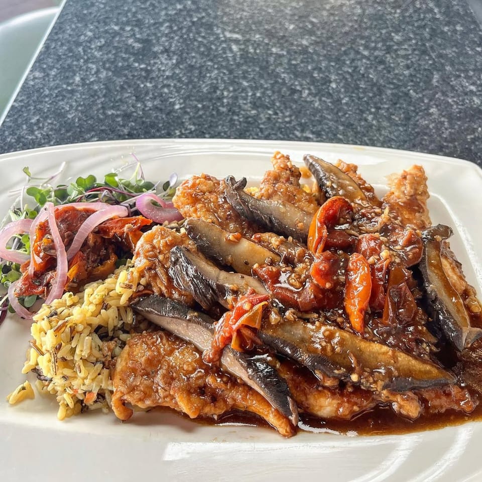 A plate of chicken with mushrooms, red peppers, wild rice, and microgreens at GS Steamers Bar & Grill.