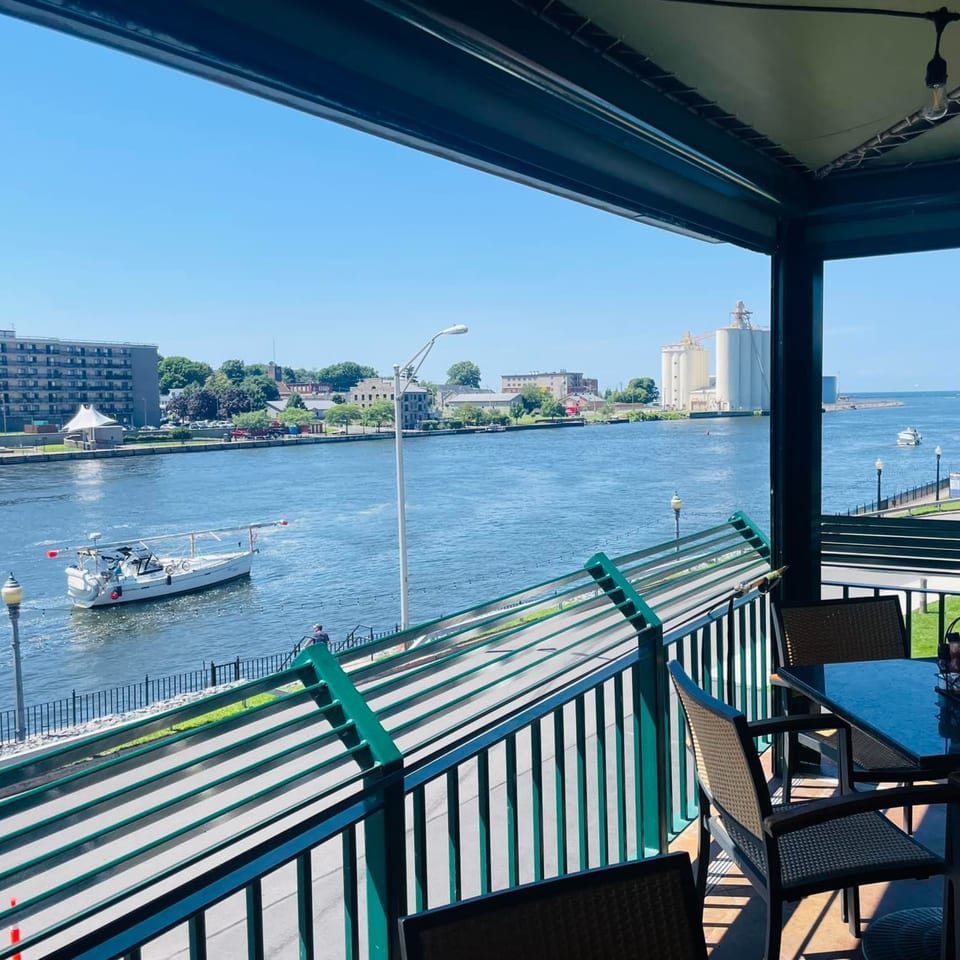 GS Steamers Bar & Grill's outdoor patio overlooking a river with boats and distant buildings.