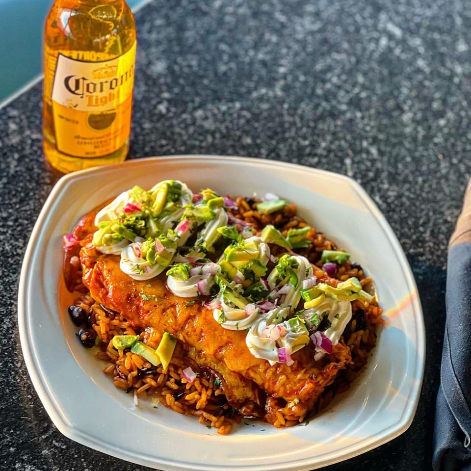 A cheesy burrito with avocado, sour cream, and red onion, served with rice and a Corona Light.