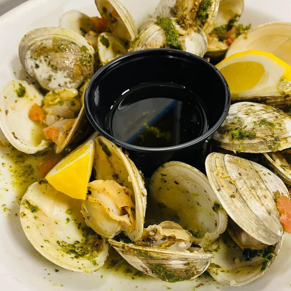 Steamed clams with green herbs, diced tomatoes, and lemon wedges, served with a black dipping sauce.