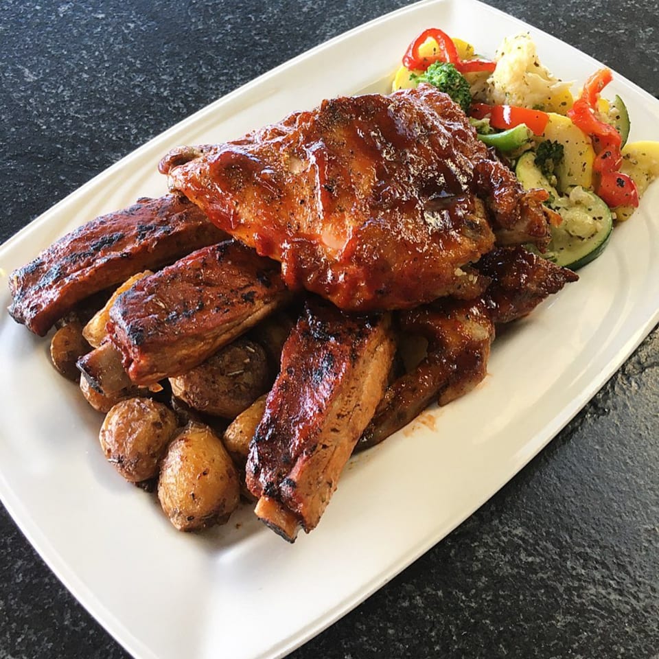 BBQ ribs with roasted potatoes and mixed vegetables on a white rectangular plate.