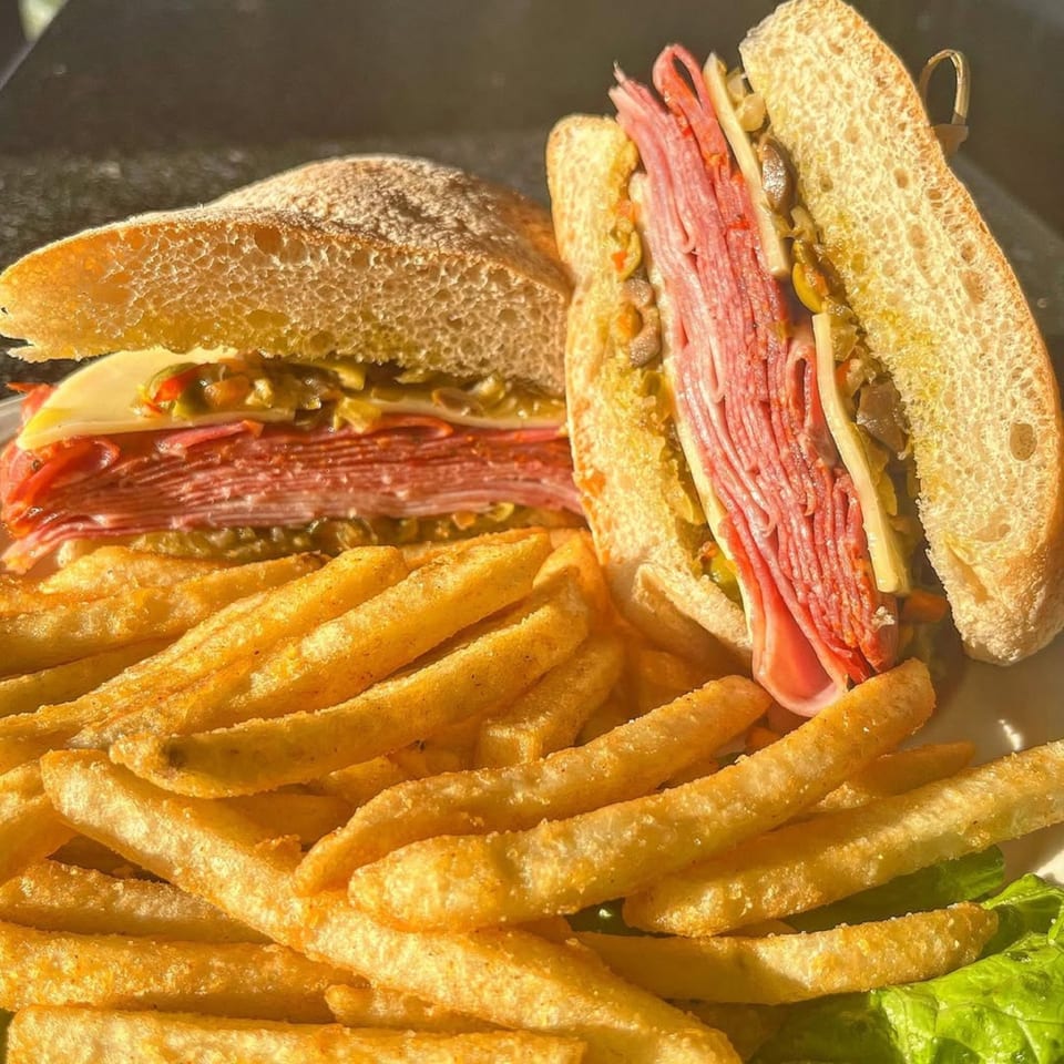 A large deli sandwich with layers of meat and cheese, served with a side of golden french fries.