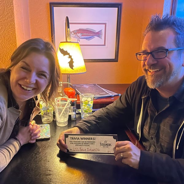 Two happy people at GS Steamers Bar & Grill holding a "Trivia Winners" voucher for drinks and pizza.