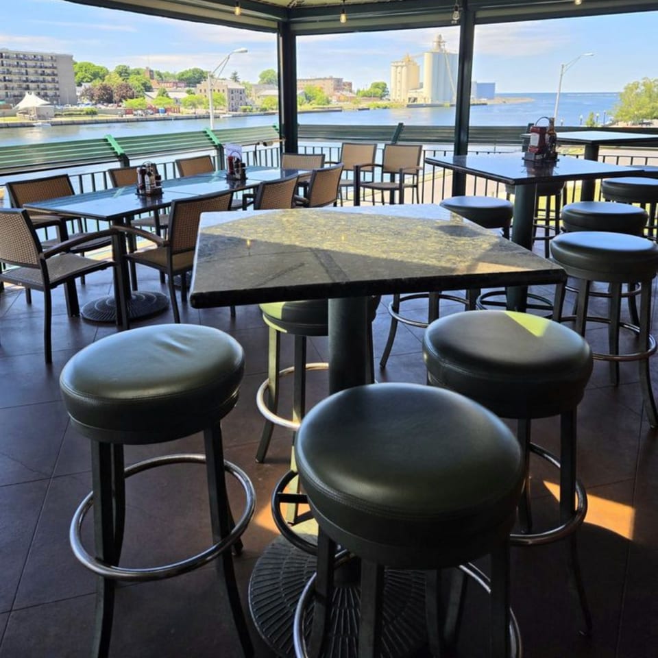 GS Steamers Bar & Grill's outdoor patio with high-top tables, stools, and a scenic waterfront view.